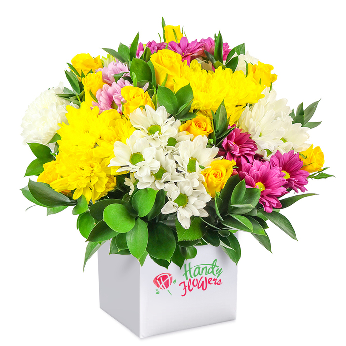 A generously full mixed bouquet rises in a rounded dome from a pristine white cube-shaped box, photographed against an all-white background that highlights every petal and leaf. Dominating the composition are sunny yellow flowers: plump chrysanthemums with many fine petals forming soft, cushion-like heads, and clusters of small yellow spray roses with buds at different stages of opening, from tight spirals to half-unfurled blooms. Nestled amongst this golden warmth are cool white daisy-like chrysanthemums with bright green centres, their simple, open faces giving the eye a place to rest, alongside fuller white chrysanthemums with a denser, more billowy form. Bold strokes of colour come from fuchsia and magenta chrysanthemums, some with hints of lighter pink at the tips, weaving through the design like ribbons and giving the arrangement a cheerful, contemporary flair that would feel perfectly at home in a modern flat near Epping Station. Rich, deep green foliage surrounds and punctuates the flowers, each leaf smooth and slightly glossy, creating a strong contrast that makes the yellows and pinks appear even more vivid, much like flowers set against the greenery of Epping Forest on a clear afternoon. The plain white box that serves as the container has clean, sharp edges and no visible decoration, acting as a neutral stage that allows the dense bouquet to take centre stage. Every bloom appears fresh and carefully spaced, showing the hand of an experienced local florist familiar with crafting budget-conscious gifts that still feel abundant and special. This arrangement would suit many occasions-birthdays, simple thank-yous, or a 'thinking of you' gesture-bringing a splash of affordable brightness to homes and offices across Epping and the surrounding villages.
