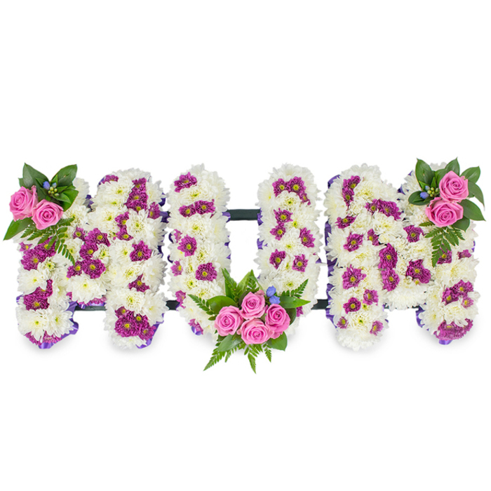 A tender, handmade floral tribute forms the word MUM in substantial, three-dimensional letter shapes placed against an uncluttered white ground so the textures read clearly. Each letter is composed from a thick cushion of snowy white chrysanthemums, their compact petals building a plush, soft surface that suggests both innocence and lasting love. Interspersed among the white are clusters of vivid magenta and purple spray chrysanthemums that add depth and a gentle cadence of colour. Vibrant pink spray roses provide focal accents: the leftmost M holds a small, elegant cluster near its upper left corner; the central U cradles a fuller bouquet of several pink roses within its lower curve; and the rightmost M echoes the left with a matching rose cluster at its upper right. Dark green foliage-varied leaves and graceful fern fronds-frames and supports each cluster, while tiny blue accent flowers are tucked in for cool contrast and a delicate finishing touch. Thin, dark connecting bars run horizontally to join the letters and keep the silhouette cohesive, and a delicate purple ribbon along the edges of each letter refines the shape. The overall mood is respectful and quietly celebratory: a classic sympathy design suited to funeral chapels, wakes, or memorial rooms near Bell Common, Epping High Street, or the quieter lanes bordering Epping Forest. A seasoned local florist would describe it as a bespoke, comforting expression of honour and remembrance for a beloved mother.