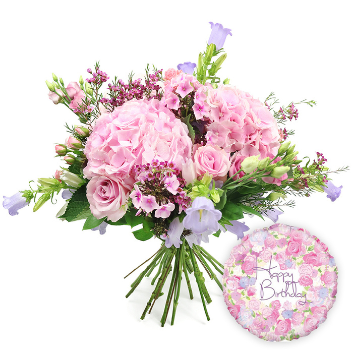 Set against a bright, uncluttered white background, this hand-tied birthday bouquet radiates a gentle, joyful energy, like a favourite café in Epping filled with soft conversation and flowers on every table. The central focus is on several large, rounded hydrangea heads in a delicate blush pink, their countless small petals forming plush, cloud-like domes that immediately suggest abundance and romance. Woven throughout these are elegant soft pink roses, some fully open with layered petals forming classic rosettes, others in earlier stages of bloom with their tips still curled inward. These roses introduce subtle variations in pink, from light shell tones to slightly warmer hues, adding depth to the arrangement. Small, intricate clusters of deeper fuchsia or magenta filler flowers-likely waxflower or a similar variety-bring a lively contrast, their tiny star-like blossoms catching the eye in between the larger blooms. Slender stems of campanula rise here and there, their bell-shaped flowers a cool lavender and periwinkle blue, giving the arrangement graceful height and an airy, garden-like charm that would feel right at home in a cottage near Epping Forest or along Bower Hill. Around the bouquet, layers of fresh greenery provide structure and balance, with a mix of broader, darker leaves and finer, lighter foliage that frames the pastel flowers and reinforces the impression of freshness. The stems, visible below, are neatly gathered and aligned, clearly showing a professional hand-tied finish, ready for delivery to a birthday celebration. To the lower right of the bouquet, a round Mylar balloon with a metallic sheen adds a playful finishing touch. Its design echoes the bouquet with a soft floral pattern in pinks, lilacs, and hints of green, and at its centre, in smooth purple lettering, the words Happy Birthday are written. This combination of flowers and balloon visually conveys a complete, thoughtful birthday surprise for someone special in Epping.