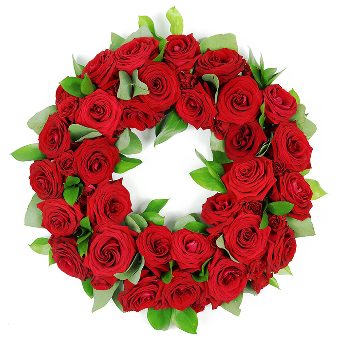 A deeply symbolic and visually arresting circular wreath, meticulously crafted from dozens of vibrant, deep red roses, rests against a pristine white background. The wreath is densely packed, showcasing a lush, opulent array of crimson blooms in varying stages of opening, from tightly furled buds to elegantly unfurled, velvety petals, each displaying rich, saturated hues and intricate folds. These abundant red roses, traditionally symbolizing love, remembrance, and respect, create a continuous, unbroken ring. Interspersed throughout the lush tapestry are clusters of fresh, glossy green foliage: broad, rounded leaves that recall eucalyptus and slender, pointed greens that offer a verdant contrast, lifting the arrangement with natural grace. The careful layering gives the piece a full, three-dimensional presence, with petals and leaves overlapping in subtle shadow and light. This red rose wreath communicates a message of solemn beauty, heartfelt emotion, and enduring tribute, a powerful visual element that resonates with memorial services, funeral arrangements, or anniversaries that honour a life lived. Set against the white backdrop, the warm crimson and cool green create a balanced, dignified harmony that feels both intimate and ceremonial. In Epping, such a wreath would be a thoughtful choice for church services, funeral director displays, or a family tribute at a graveside, conveying sympathy with quiet eloquence. Crafted by a skilled local florist, it embodies the care and artistry of a local florist, offering a timeless sign of condolences, respect, and remembrance for the community.
