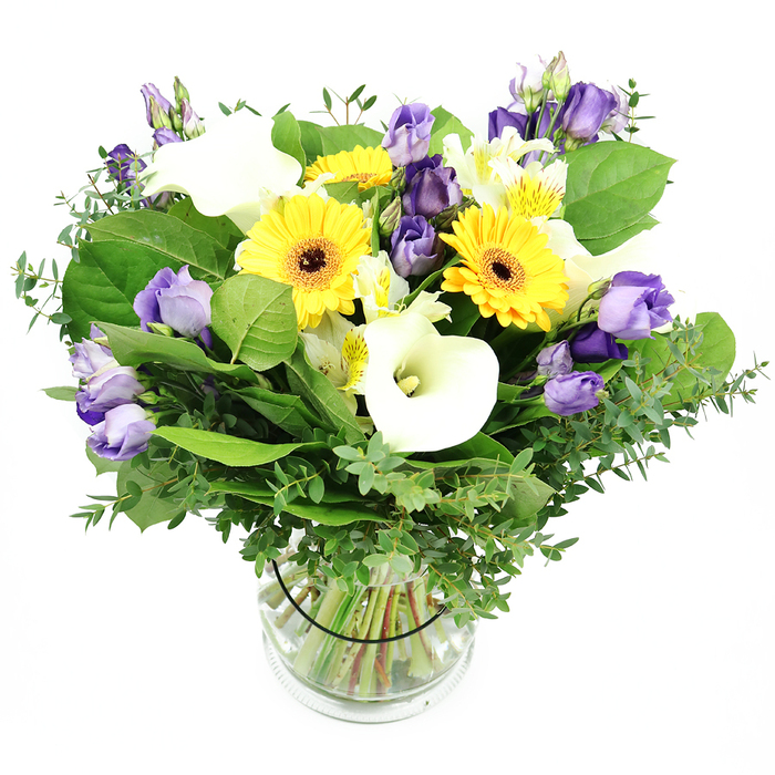An artfully staged mix of sunshine and shade, this bouquet is a classic study in contrasts and grace, arranged in a clear glass cylinder by a seasoned local florist in Epping. The eye is drawn first to the bright yellow Gerbera daisies, their broad petals around dark centers that echo summer suns. White Calla lilies rise with architectural elegance, their smooth curves contrasting with the lilac and purple Lisianthus that cluster nearby in soft, ruffled blooms, some fully open, others in delicate bud form. Interleaved white Alstroemeria bring micro-streaks of yellow and green, like careful brushwork. A lush bed of greenery-feathery eucalyptus for lift and silvery gleam, plus deep green leaves for fortitude-gives the arrangement a generous, garden-fresh feel. The transparent vase reveals neatly trimmed green stems submerged in crystal-clear water, and a slender black band holds the stems in graceful alignment. The bouquet radiates joy, purity, and refined elegance, making it an ideal gift for celebrations, birthdays, or a thoughtful gesture delivered to homes along Epping High Street or the town's leafy lanes. Its pristine presentation, against a clean white background, makes it equally at home in a modern apartment or a country-style dining room, a testament to the florist's craft and to the town's appreciation for fresh, seasonal color.