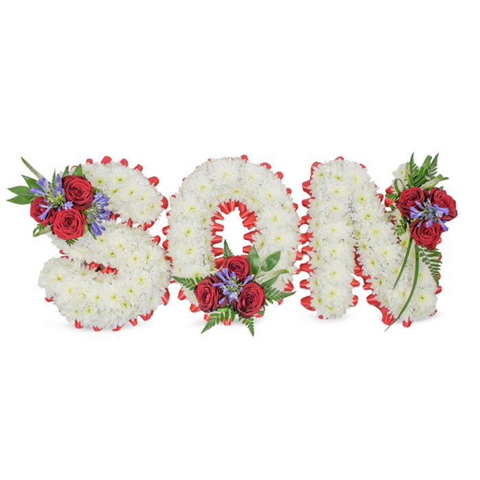 A poignant, personalised funeral tribute spells SON in bold capital letters arranged on a clean white surface. Each character is densely formed from pure white chrysanthemums, their many small blooms packed to create a soft, even, cloud-like texture that reads with quiet dignity. Encircling each letter is a vivid red satin trim, folded into a scalloped, pleated border that neatly defines every curve and corner-especially evident in the S's sinuous turns, the O's inner loop, and the N's upright stems. Three carefully placed clusters of accent blooms lift the composition: the S bears its cluster on the upper-left curve, the O carries a modest spray at its bottom centre, and the N is ornamented at its top-right. These groupings combine velvety deep-red roses with upright, blue-purple spikes (suggestive of Liatris or similar flowers) and a tapestry of dark green foliage including fern-like fronds and soft trailing leaves. The contrast of immaculate white, passionate red and contemplative blue-purple creates an emotional palette of purity, enduring love and remembrance. The texture of the chrysanthemums against the glossy ribbon is tactile in spirit; the roses add a plush, familiar scent while the Liatris spikes bring a delicate, architectural verticality. Presented in gentle daylight that removes harsh shadows, the piece reads as a classic, bespoke tribute-suitable for a funeral service, wake or graveside near Epping's community churches and green spaces. A seasoned florist's attention to balance, proportion and botanical choice is evident in the precise ribbon pleating and the tasteful placement of each accent cluster, offering a dignified farewell to a cherished son.