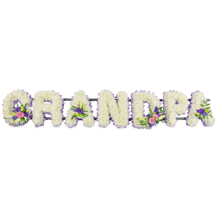 This photograph captures a classic GRANDPA floral name tribute, arranged horizontally so that each capital letter stands clearly defined and full of life. The base of every letter is densely packed with small, white chrysanthemum blooms, their round petals overlapping to form a plush, cushion-like surface that feels both soft and reassuring. Framing this white canvas, a narrow band of delicate purple and lilac flowers runs along the edges, creating a gentle outline that helps each letter stand out without overpowering the calm, peaceful mood. The letters are discreetly supported by a slim dark green framework that runs behind them, almost hidden from view, ensuring the word appears as one continuous, flowing tribute. Carefully placed accent clusters break up the expanse of white in a thoughtful, balanced way. On the 'G', a small spray of flowers combines a graceful white lily-style bloom, bright pink and fuchsia heads, and hints of deeper purple, all nestled into fresh green foliage. The first 'A' mirrors this with a slightly smaller grouping, while the 'D' features a more pronounced cluster, including touches of lime-green button chrysanthemums that bring a subtle spark of colour. Another 'A' is softly embellished with similar pink and purple notes, connecting the design from left to right. The arrangement sits against a plain white background under soft, even lighting, drawing the eye to the craftsmanship and respect in every detail. It feels like a deeply personal farewell for a grandfather-something a family in Epping might choose for a service at the local crematorium or a quiet ceremony near the High Street-where flowers stand in for words that are too hard to say.