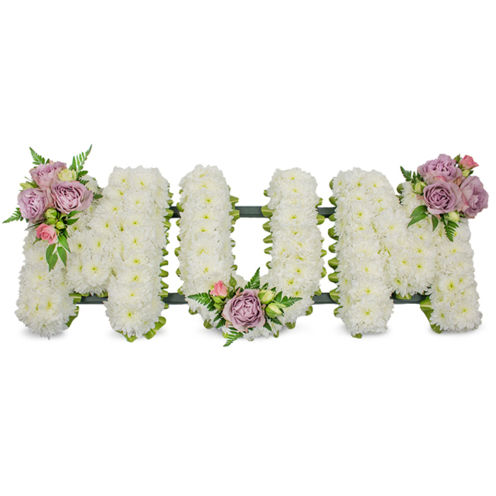 A lovingly made tribute spelling MUM in large, free-standing letters, entirely covered in thousands of small, fresh white chrysanthemums that create a soft, even surface reminiscent of a downy white blanket. The close-packed blooms reflect cool, steady light, producing a serene, almost luminous effect that feels respectful and calm. Three tasteful accent clusters of soft lavender roses and pale pink rosebuds have been artfully positioned to catch the eye: one graces the upper left arm of the first 'M', another nestles in the central curve of the 'U', and the last sits on the upper right arm of the finishing 'M'. The roses range from open blooms to tight buds, offering both the fullness of memory and the delicacy of a private sentiment; their gentle fragrance is suggested rather than overpowering. Fresh, vibrant greenery - slender fern fronds and lighter green leaves - weaves through the composition, adding contrast, movement, and natural depth against the white chrysanthemum field. A dark green structural element, possibly a ribbon-wrapped bar or mossed foam base, is visible at the letters' bases, providing discreet support and a clean line that unites the trio. Presented against a pristine white background, the arrangement conveys peace, reverence, and the quiet dignity of a mother's memorial. As an Epping florist familiar with local funerals near Epping Forest and the High Street chapels, Flowers Epping (flowersepping.pro) would describe this piece as a tender, traditional choice - perfect for a funeral service, wake, or graveside dedication where the family wants a calm, loving statement of remembrance.
