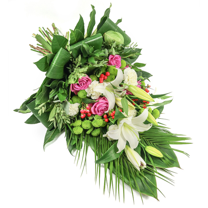 Arranged with expertise by Epping's local florists, this elongated cascading funeral spray stretches diagonally across a white background, each element thoughtfully placed to convey serenity and respect. The centrepieces are large, fragrant white lilies-some wide open to reveal pale yellow stamens, others partially closed, promising future blooms. Interlacing them are deep pink and fuchsia roses at varying stages of bloom, their velvet petals symbolising affection and remembrance. Pockets of ruffled white carnations bring fullness and softness, while lime-green button chrysanthemums form striking, rounded mounds, lifting the visual scheme with their contemporary feel. Vibrant red hypericum berries provide flecks of bright colour, drawing attention and offering a gentle contrast amid the tapestry of green foliage. The backdrop is a layered ensemble of dark green glossy leaves-some folded, as if sculpted for drama-intermixed with lighter, feathered greens and slender palm fronds that cascade toward the lower corner, amplifying the arrangement's sense of movement and flow. Local touches-a palette inspired by Epping's woodland edges, an airy fullness reminiscent of open Essex landscapes-give the spray a sense of place and authenticity. Designed for moments of tribute and remembrance, this lush composition is an eloquent gesture for funerals, memorials, or quiet condolences, blending time-honoured tradition with fresh, nurturing beauty from the heart of Epping.