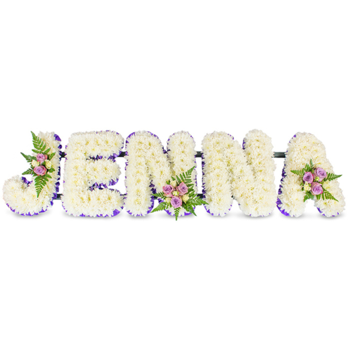An elegant, personalized memorial display spells the name JENNA in large, three-dimensional uppercase letters, each letter densely covered in creamy-white chrysanthemums or similar small florets to create a soft, voluminous surface reminiscent of a cloud. A rich purple ribbon-like trim outlines the interior edges and base of each letter, giving crisp definition and a subtle, respectful pop of colour against the otherwise immaculate white. Artistic clusters of blush and lavender spray roses, accompanied by a few pale cream roses and finely textured fern fronds, are positioned with considered symmetry - one on the sweeping upper curve of the J, another on a central N, and a final cluster on the right-hand curve of the A - adding warmth, scent and a natural counterpoint to the formal lettering. The letters are joined by thin, dark connecting bars that provide structure without distracting from the floral surface, so the piece reads as a cohesive name tribute suitable for placement by a casket, memorial table or chapel lectern. Under soft, even lighting the chrysanthemums' tiny petals pick up a faint sheen while the coloured roses offer gentle highlights; the overall scent is a mild, comforting mix of chrysanthemum freshness and rose sweetness. Crafted with careful spacing and durable construction, this tribute offers a deeply personal way to remember someone in Epping and the surrounding parish, and it sits well alongside floral tributes delivered to local funeral directors or placed for a service near Epping Forest.