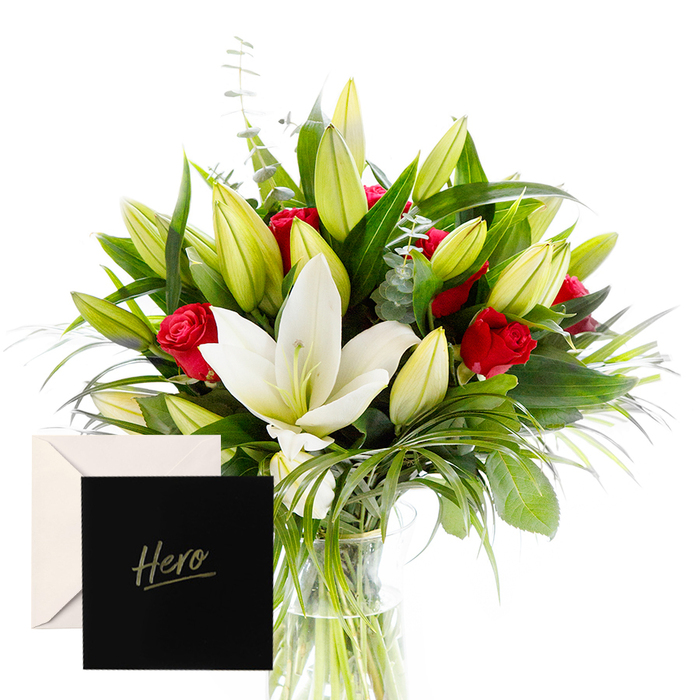 As the florist, there is joy in blending the bold with the serene, and this arrangement is a testament to that harmony. White lilies drift at the heart of the bouquet, luminous and airy, their satin petals contrasting splendidly with the tactile, lush greenery that encircles them. Rich ruby roses punctuate the design, each one a symbol of love and respect. The verdant leaves provide a cooling, almost forest-like backdrop, while unopened lily buds suggest anticipation and new beginnings. In soft, natural light, the bouquet feels alive and uplifting-perfect for honouring someone's strength or celebrating a significant achievement. The accompanying 'Hero' card makes this gesture intimate and enduring. In Epping, you can imagine it brightening a living room after a town council meeting or marking a milestone with a friend who calls the town home. Our team at Flowers Epping crafts each stem with restraint and care, ensuring the fragrance travels through the room and lingers. Delivered across Epping and nearby areas, this bouquet carries a quiet confidence that speaks to resilience and gratitude.