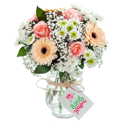 Close your eyes and imagine the soft rustle of leaves in Epping Forest at dawn, and you can almost sense the inspiration behind this sophisticated bouquet. At its center are classically beautiful peach-pink roses, each petal layered in plush spirals, radiating a gentle, romantic aura. Flanking these are two showstopping gerbera daisies in hues of soft peach, their vivid centers deepening the composition's drama. Wisps of white gypsophila seem to float between the blooms like woodland mist, infusing the bouquet with an airy lightness, while clusters of white chrysanthemums, lively with green centers, add both texture and a fresh springtime vibration. Here and there, deep green leaves are tucked thoughtfully for a touch of nature's grounding presence. The stems are gathered in a clear, textured glass vase filled with water, its simplicity echoing the rural charm of Epping's countryside. Around the vase's neck, a length of natural twine holds a small white tag, always ready to accompany congratulatory wishes or heartfelt thanks. This bouquet is a perfect gesture for any Epping home, channeling both serenity and quiet optimism.