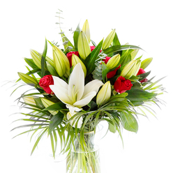 A refined studio-style bouquet arranged in a transparent cylindrical vase, pictured on a bright white background so every petal and leaf stands out. Dominating the scene is a single, noble Oriental lily in full creamy-white bloom: its pristine petals unfurl smoothly to reveal pale yellow stamens and a delicate green pistil, a serene centrepiece that feels both pure and ceremonial. Encircling the open lily are numerous lime-green and soft yellow lily buds at varying stages, their tight forms promising new blooms and lending the composition natural volume. Among these are clusters of small, velvet-red rosebuds and partially opened roses, each one a rich, passionate counterpoint to the lighter tones. The arrangement is built on a variety of lush foliage - deep, forest-green lily leaves that give weight and backdrop, long, arching palm fronds that add texture and movement, and rounded, silvery eucalyptus leaves that bring a cool softness to the palette. The clear vase shows clean green stems submerged in fresh water, reinforcing the bouquet's crisp freshness. The overall feeling, caught in the studio light, is of polished simplicity: fragrant yet restrained, ideal for marking anniversaries, congratulations, or moments of heartfelt affection. As a local touch, this is the kind of arrangement our team at Flowers Epping often prepares for customers walking off the High Street or collecting after a visit to Epping Forest - a classic pairing of white lilies and red roses made with steady craft and attention to scent, texture, and balance for recipients across Epping and nearby villages.