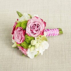 Laid gently on a pale, textured fabric that suggests natural linen or soft burlap, this compact bouquet looks as though it has just been set down between photographs at an Epping wedding. Two lush pink roses draw the eye first, each bloom fully open yet still holding a sense of promise in their intricately layered centres. Their petals blend from a tender shell-pink at the heart to deeper fuchsia tones along the edges, where the colour intensifies into a fine magenta rim. Tucked closely around them are rounded tufts of vivid lime-green button chrysanthemums, their many tiny petals forming tight, cushion-like spheres that contrast playfully with the smooth rose petals. Threaded throughout the arrangement, small white and cream flowers-likely lisianthus, freesia, or delicate waxflower-soften the palette, their star-shaped blossoms and tiny yellow centres catching the light and giving the bouquet a fine, lacy texture. Hints of dark green foliage peek from beneath, providing quiet structure and framing the brighter tones. The stems are clipped short and gathered into a tidy cluster, firmly wrapped in a vibrant fuchsia satin ribbon that mirrors the richer notes in the roses. A slender strand of white faux pearls spirals gracefully around the handle, creating an elegant, jewellery-like detail that feels made for a bridesmaid or bride. The soft, even lighting emphasises freshness and colour without harsh shadows, as if the bouquet has been photographed in gentle daylight filtering through a window above Epping High Street. It evokes a mood of poised celebration, suitable for local ceremonies, intimate engagement parties, or same-day wedding delivery across Epping.
