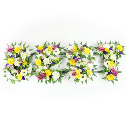 Presented against a stark white studio background, this substantial floral lettering spells BEST in four individual, three-dimensional characters crafted from an abundance of freshly cut flowers and lush foliage. Dominant notes of sunshine yellow-seen in long-stemmed roses and cheerful gerbera daisies-are balanced by creamy white chrysanthemum-type flowers and velvety spray carnations, producing a bright, comforting palette. Deeper accents of soft lavender and rich purple lisianthus are tucked into the composition to add thoughtful contrast and visual depth, while pops of vivid magenta-pink from small spray roses or carnations lift the arrangement with joyful energy. Fine clusters of pale green and white filler flowers provide subtle texture and help the eye travel across each letter; generous fern fronds frame and soften the shapes, their dark green fronds giving a natural, leafy silhouette. Where the blooms part slightly you can glimpse the dark green or muted metal support rails that keep each letter structurally sound. Shot front-on with clear, balanced light, every petal shadow and glossy leaf is visible, evoking the fresh, slightly sweet scent of roses layered with the earthy green of ferns. As a local florist piece intended for sympathy or celebration alike, this tribute could be delivered to services at nearby venues, from Epping High Street chapels to gatherings in the shade of Epping Forest. Flowers Epping prepares such hand-crafted memorials with steady hands and an eye for proportion, offering careful placement and local delivery across the Epping area.