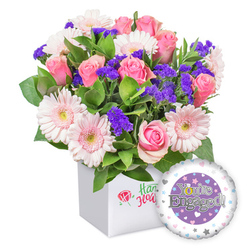 From the soft morning light along Epping's High Street to the scent of fresh blooms, this joyful bouquet radiates celebratory charm. Pink roses unfurl in creamy spirals, their petals a timeless symbol of romance, while moonlit gerberas in pale blush lend airy lift with crisp white edges and pale yellow centers. Intertwined among the blooms, deep purple statice provides a vibrant texture, like whispered promises, and generous green foliage spills over the clean white square box, giving the arrangement a garden-fresh feel. The bouquet rests in a snowy white presentation box that emphasizes contemporary elegance, its front bearing a subtle emblem rather than a loud logo, hinting at the florist's quiet craftsmanship. To the side, a round engagement-themed foil balloon glows: its purple central panel carries the silver proclamation 'You're Engaged!', with the 'O' cleverly rendered as a golden engagement ring. The outer white rim is dotted with tiny pastel hearts and delicate silver stars, completing a mood of romance and joy. Crafted by Flowers Epping for couples across Epping, Buckhurst Hill, Loughton, and the surrounding locales, this arrangement is perfect for proposals, anniversaries, or heartfelt congratulations. It brightens a room with a soft, friendly glow and is well suited to same-day delivery to homes, offices, or event spaces across the district, bringing a bright touch to any celebration.