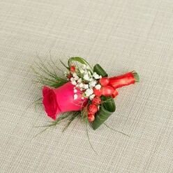 A finely crafted boutonniere rests gently on a pale beige, textured fabric backdrop, the subtle weave reminiscent of natural linen often seen in relaxed yet refined weddings around Epping. The central star is a single fuchsia pink rose, its petals densely layered and slightly cupped, giving an impression of lush, velvety fullness ready to open just a little more. Surrounding this romantic bloom, clouds of white baby's breath scatter like tiny pearls, lending an airy, innocent quality that softens the vivid pink. Nestled among the gypsophila, plump red hypericum berries gleam with a lacquered shine, introducing a festive note and drawing the eye with their rounded shapes. Fine, feathery greenery, similar to asparagus fern, stretches outward in delicate sprays, while darker, broader green leaves are deliberately curled and arranged to frame the rose and steady the composition. The stems are gathered and wrapped with a length of red satin ribbon, its smooth, lustrous surface catching the light and tying the entire palette of pink, white, red, and green together. From the overhead viewpoint, every detail is visible: the layered textures, the contrast between matte petals and glossy berries, and the precise way the ribbon is secured. It is easy to imagine this buttonhole being pinned to a groom's suit on his way from a home near Epping Forest to a ceremony nearby, a small but significant floral detail designed to celebrate love, commitment, and the heartfelt moments of a wedding or formal event.