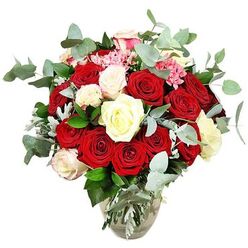 This image shows an opulent, full-bodied rose arrangement, styled with the care of an experienced local florist and photographed against a pure white backdrop to highlight every colour and curve. A clear glass vase, slightly bulbous at the base and tapering gracefully towards the rim, anchors the bouquet and reveals the straight, freshly cut stems gathered neatly in cool water. Rising from the vase, the flowers form a generous, rounded canopy of predominantly red roses in rich, romantic tones-from deep crimson to bright scarlet. Some blooms are tightly furled buds, others half-open, and many fully expanded, with soft, velvety petals layered in concentric circles that invite the touch. Interspersed among these passionate reds are clusters of white and creamy ivory roses, along with a scattering of ivory blooms tinged delicately with blush pink at the edges, lending a sense of softness and refined charm. Tiny bright pink filler flowers, possibly mini carnations, nestle between the larger roses, adding a sparkling lightness and a playful, almost confetti-like effect. Blue-green eucalyptus sprigs arc through the design, their distinctive round leaves and slightly frosted finish echoing the cool, calm atmosphere of early mornings around Epping High Street or the edges of Epping Forest. Dark green foliage and subtle silvery leaves provide additional depth, making the bouquet look abundant and expertly balanced from every angle. The pristine background ensures no distractions, so the eye rests solely on the rich colours and textures, suggesting a bouquet perfect for romantic deliveries across Epping-whether it is a surprise anniversary gift, a grand Valentine's gesture, or a special way to transform a living room into a place of celebration.