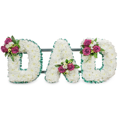 A thoughtfully handcrafted sympathy tribute spells out DAD in three substantial capital letters, each letter completely covered with tiny, immaculate white chrysanthemums for a plush, velvety surface that reads as purity and peace. The white blooms are arranged with close attention to texture and volume so the faces of the letters read as soft, uninterrupted panels. An emerald-green ruffled ribbon crisply lines the outer and inner edges of each character, its cool tone setting the white off with solemn refinement. Behind the letters a discreet, dark green or grey horizontal bar provides support, keeping the ensemble steady for display at a memorial service or graveside. Each letter carries a small, lovingly arranged bouquet of accent flowers: the first D features a cluster of rich magenta roses and white freesia on the upper left curve; the A cradles its cluster in the lower central V; the second D is balanced by a matching spray on the upper right curve. The roses bring a deep, warm colour that reads as affection, while the freesia's delicate white blooms and the lush dark foliage add freshness and depth. The composition looks as though it were prepared for a dignified service in Epping - perhaps for viewing at a chapel near Station Road or a quiet ceremony by the trees of Epping Forest - and carries a tone of loving farewell. The arrangement's clean lines, soft scents, and tactile fullness make it a classic choice to honour a beloved father with quiet dignity.