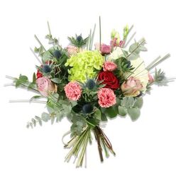 This hand-tied arrangement reads like a small, fragrant garden gathered into a neat bundle and set against a brilliant white backdrop so every hue and form is clear. The dominant, lime-green hydrangea at the heart of the bouquet has a cloud-like volume of tiny petals that creates an immediate focal point; around it, soft peachy-pink and cream roses open with a gentle, classic romance while deeper red roses add weight and elegance. Coral-pink carnations, their edges crinkled and lively, introduce warmth and casual charm, and a scattering of blue-grey Eryngium thistles cuts through the softness with a modern, architectural note - spiky, star-shaped heads that catch the eye and provide pleasing contrast. Ample greenery, especially round, silvery eucalyptus leaves, frames the blossoms with a contemporary, aromatic curtain, while thin blades of bright green grass and other filler stems reach up and out to lighten the silhouette. The stems are neatly gathered at the base and bound with a natural twine, the cut ends visible and fresh, conveying careful handcraft and same-day readiness. Imagine receiving this bouquet after a walk across the nearby fields of Epping Forest or picking it up following a morning browse at the town market - it smells faintly of rose and eucalyptus, feels textural under the hand, and suits both casual celebrations and more formal moments. The composition balances plush romance with a touch of wildness, making it an excellent choice for anniversaries, a thoughtful thank-you, or a brightening centrepiece in a contemporary home.