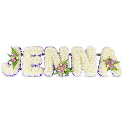 A lovingly constructed floral tribute reads JENNA in bold, three-dimensional capitals, each letter formed from hundreds of small, snowy-white chrysanthemums or similar tiny blooms, shown against a pristine white background that amplifies their soft texture. A narrow lilac-purple border hugs the inner curves of every letter, acting like a quiet frame and lifting the letters from the white field. Small, carefully placed sprays of pale pink and lavender spray roses, with touches of cream roses and fresh fern fronds, decorate the J, a central N and the final A, punctuating the steady white surface with gentle colour and organic rhythm. The letters are subtly linked by slender dark bars for stability, allowing the piece to stand or to be mounted for viewing at a funeral venue. The floral work emits a mild, comforting rose-tinged scent under soft light that reveals the petals' fine texture and the meticulous wiring beneath. Designed for sympathy and remembrance, this custom name tribute is the sort of piece we prepare for local services around Epping High Street, St. John's Church, or for families arranging wakes near Epping tube station; as Flowers Epping we take care to balance readability, resilience, and tenderness when creating letters like this. The overall impression is solemn yet tender: a bespoke, name-bearing memorial arranged with restraint and dignity to honour a loved one's memory.