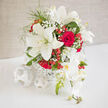 A luxurious wedding arrangement of snowy white lilies, classic red roses, and softly cascading orchids rests in a simple white woven vessel, the entire design shaped into a generous, rounded dome that feels abundant yet composed. The lilies stretch open with wide, star-like faces, their creamy petals edged with the faintest hint of shadow, while the red roses nestle in between, their spiralling centres full and velvety, like whispered promises. Pale orchid blooms trail just slightly over the rim, introducing a gentle, flowing line that leads the eye downward, as if the bouquet is in motion. Sprays of baby's breath are threaded delicately throughout, softening the contrast between red and white and giving the composition a light, airy halo. Coral-red hypericum berries punctuate the design, round and glistening, echoing the joyful feel of wedding celebrations in Epping, perhaps after a ceremony near the historic St John's Church or a reception overlooking the greenery that borders Epping Forest. The soft, natural lighting casts subtle highlights on the smooth petals and the textured weave of the container, enhancing every curve and fold without harshness. This is a bouquet created to sit beautifully at the centre of a wedding table, a registrar's desk, or a top table at a local hotel, radiating warmth and romance. The imagined fragrance is a blend of lily sweetness and the deep, comforting scent of roses, a perfume that lingers gently, much like the memories of the day itself. Every stem has been positioned with care, giving the impression of effortless elegance born from true florist craftsmanship.