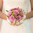 On a serene Epping wedding morning, a bride rests her hands upon a bouquet as softly enchanting as the mist above Epping Forest. Glowing in diffused daylight, the bouquet's dreamy, mauve-pink roses unfold in gentle spirals, their fuchsia-fringed petals echoing the blush of young love. Between them nestle lively lime-green button chrysanthemums, creating a crisp counterpoint, their fresh, rounded forms reminiscent of dew-kissed lawns in Stonards Hill Park. Snow-white clusters of petite flowers-perhaps freesia or waxflower-encircle the bouquet, threaded with emerald buds and leaves that add depth and vigor. The bride's nails, painted in subtle pink with a single sparkling accent, cradle these blooms with quiet joy. The intricate lace overlay of her elegant off-white gown peeks through, weaving texture and tradition into the scene. This artfully composed arrangement, likely from one of Epping's esteemed florists, honours the timeless romance and anticipation surrounding a wedding day. With every petal and ribbon of light, the bouquet speaks of purity, new beginnings, and the art of local floral design, perfectly at home in elegant ceremonies across Epping's historic venues.