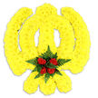 This striking, large floral sculpture is built from countless small, tightly clustered bright yellow chrysanthemums that form a bold, stylised figure against a clean white backdrop. The overall silhouette is rounded at the centre with two prominent upward curving lobes, giving it a friendly, almost character-like presence reminiscent of a simplified cartoon bird or beloved yellow mascot, while remaining clearly an artful floral creation. The dense yellow blooms create a plush, tactile surface - soft to the eye, with petals that catch the light and suggest a gentle, sunlit warmth. Anchoring the composition at the lower centre is a compact, dramatic cluster of five deep red roses, each bud arranged precisely and framed by rich, dark green fern fronds; the contrast between the glossy, velvety rose petals and the feathery greenery makes the focal point read instantly as a heart of reverence. A faint grey shadow beneath the piece gives a subtle sense of depth and confirms it as a freestanding tribute likely crafted for a special event, memorial display, or playful but respectful celebration. The scent is understated - a clean, floral lift of chrysanthemum sweetness beneath the classic perfume of the roses and a faint green, fern-like freshness. As a local florist in Epping I often sketch similar bespoke pieces for themed funerals, pop-culture commemorations, or sympathy displays delivered to homes and venues around Epping High Street, St. John's and the edges of Epping Forest. The workmanship shows careful hand-placing of each bloom to maintain the emblematic curves and the emotional balance between bright hope and dignified remembrance, making it both an artistic statement and a comforting memorial element for family and friends.