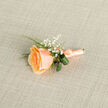 Presented in a clear, close-up view, this buttonhole is a study in soft colour and restrained elegance, the sort of piece we prepare by hand at Flowers Epping for weddings and special ceremonies around Epping High Street and Bell Common. At its heart sits a single apricot-peach rose, petals tightly coiled at the centre and unfurling outward in layers that shift from warm orange-amber toward cream, their edges catching light like brushed silk. Delicate sprigs of white gypsophila nestle against the rose, their tiny blossoms offering an ethereal, veil-like contrast that lifts the composition. Bright, narrow blades of grass extend with fresh, linear movement while two deeper green, rolled leaves are tucked in to give weight and an artful silhouette. The stems are wrapped with a coordinating peach satin ribbon, finished in a small, neat bow whose sheen mirrors the rose's softness; a subtle metallic pin sits near the base so the boutonniere can be secured to a lapel. The arrangement is placed on a light beige linen background with a fine cross-hatch texture, the neutral field ensuring every fold and petal reads clearly. There's the faint impression of citrus-rose fragrance and a gentle tactile invitation in the satin wrap - qualities I note when preparing buttonholes for grooms walking from Station Road to a ceremony beneath the canopy of Epping Forest. It's designed to be elegant, reassuring, and quietly celebratory.
