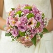 This enchanting bridal bouquet, freshly arranged in Epping, unfurls in a tapestry of pastel roses, lively green button mums, and whimsical accents, echoing the gentle romance of a local spring morning. Soft lavender and blush pink roses anchor the design, their fragrant petals opening gracefully with the promise of a radiant day. Intertwined are clusters of lime green button chrysanthemums, each one a burst of brightness that enlivens the bouquet and lends it a playful, modern twist, reminiscent of the vibrant community spirit at Epping's weekly markets. Pink alstroemeria, with delicate streaks of yellow and deep maroon, peek out from the arrangement, offering a hint of the exotic and conjuring memories of joyful celebrations with friends and family gathered in the town's picturesque venues. Tiny, cloud-like sprays of white baby's breath impart an ethereal softness, weaving gently through the bouquet and infusing it with a sense of innocence and poetic grace. Glossy dark green leaves frame the flowers, grounding the colours and highlighting the lushness at the heart of Epping. The bouquet is softly illuminated, held lovingly against the lace of the bride's dress as her hands cradle the stems, symbolising tenderness and hope. This is more than a collection of florals; it's a handcrafted expression of joy and new beginnings, thoughtfully designed for weddings in Epping, where tradition mingles with contemporary flair and every detail is chosen with heartfelt care.