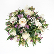 Laid out against a bright white background and viewed from above, this bouquet has the serene feel of a gentle echo, calm and contained, as if resting in a quiet room overlooking Epping's leafy streets. The flowers are gathered into a rounded, compact shape, centred around a cluster of creamy white roses. Each rose is lush and carefully formed, its petals soft and velvety, unfurling from a tight spiral into broader, cupped shapes. At the heart of several blooms, the colour deepens delicately to pale ivory and a hint of warm peach, giving a sense of depth without disturbing the tranquil palette. Threaded through the roses are slim stems of purple alstroemeria buds, most of them still tightly wrapped. Their surfaces carry a gentle gradient of colour, from dusky lavender at the tip through muted mauve to a subtle green near the base, some showing faint streaks along the bud. Between these larger forms, small-flowered baby's breath scatters points of pure white, light as breath on a cold morning walk near Epping Forest. The surrounding greenery is rich and steady, with broad, deep green leaves that cradle the blooms and complete the softly domed silhouette. Their smooth, slightly glossy surfaces catch the light in a quiet way, adding texture rather than drama. The overall impression is one of poised comfort and understated grace-a bouquet that seems made for offering sympathy, perhaps delivered gently by a local Epping florist to a home or chapel, where its calm presence can speak when words are hard to find.