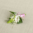A single handcrafted boutonniere lies against a natural oatmeal-coloured woven fabric, its soft texture echoing the calm of a quiet afternoon near Epping Forest. The focal bloom is a creamy white alstroemeria, petals open and velvety, each inner petal traced with fine maroon-brown speckles that add depth and character. Clustered closely around it are several smaller white blossoms, some still in bud, others just beginning to unfurl like tiny bells, reminiscent of delicate campanula or lily-of-the-valley. Wisps of white baby's breath drift between them, creating a light, misty halo that softens the edges and lends a dreamy, ethereal feel. To one side, a striking elongated cone of bright green buds, likely ornithogalum, introduces a bold, sculptural line that keeps the design feeling modern and fresh. Dark green foliage fans out behind the flowers, broad leaves providing a lush backdrop while fine, looping strands of bear grass curl and arc over the composition, adding movement and a touch of playful spontaneity. At the base, the stems are carefully wrapped in a pale pink satin ribbon, tied into a petite bow whose glossy finish catches the light, suggesting celebration and joy. The entire piece feels like it has been composed with great care by an experienced Epping florist, ideal for a wedding at a local church, a prom at a nearby school, or a special family gathering. It radiates a sense of purity, gentle hope, and quiet elegance, like a tender gesture captured in flowers and ribbon.