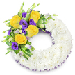 A deeply significant floral tribute shaped as a perfect 'O', this circular wreath reads at once as a quiet emblem of remembrance and a handcrafted statement of care from the heart of Epping. The main body of the ring is formed from hundreds of small, pristine white spray chrysanthemums packed tightly together so that their many layered petals create a plush, cloud-like surface; the texture appears almost velvety to the eye, softening light and suggesting calm. Crowning the upper-left curve is a considered cluster of colour - several fully opened yellow roses with warm butter-to-gold petals, their soft fragrance imagined even from the image, sit alongside rich, royal purple lisianthus whose ruffled, cup-shaped blooms lend a satin coolness to the palette. A few pale lavender lisianthus buds and tender green shoots tuck into the spray, adding natural depth and suggesting slow, hopeful opening. Interspersed foliage - glossy oval leaves, faintly variegated greens and delicate fern fronds - provides structure, contrast and a garden-fresh softness that frames the vivid roses and lisianthus. A narrow, dark purple mesh ribbon peeks subtly from beneath the white chrysanthemum ring along both inner and outer curves, quietly echoing the purple blossoms and finishing the piece with a refined touch. Photographed against a clean white background, the wreath's open centre and balanced asymmetry communicate respectful solemnity while the yellow accents introduce warmth. This is a funeral tribute designed to convey peace, gentle farewell and enduring beauty - the kind of arrangement you might see laid at a service in St John's or near the trails of Epping Forest, crafted with steady skill and thoughtfulness.