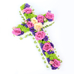 A lush floral cross is displayed on a spotless white background, its generous size and diagonal tilt giving it a strong visual presence, as though it has just been laid with care in a peaceful Epping church. The cross is fully covered with flowers, leaving no gaps, which gives it a sense of abundance and devotion. Along the outer edge, tiny white spray chrysanthemums are packed tightly together, creating a continuous, cloud-like frame that softens the strong lines of the cross. Just beneath this border, a neatly folded band of pale green ribbon or foliage wraps around, offering a refined, tailored touch and a gentle nod to the green spaces and woodland that surround Epping. Inside this frame, the main body of the cross is alive with colour. Oversized roses in bright fuchsia pink and gentle creamy yellow bloom fully, their velvety petals unfurling to reveal intricate centres. These roses are spaced with intention, marking key areas along the length and arms of the cross. Between them, clusters of lime-green button chrysanthemums provide playful, spherical bursts of texture, bringing freshness and energy. Threaded throughout the design are smaller blooms in deep purple and violet tones-likely lisianthus or statice-which add shadows, depth, and a slightly more contemplative mood. The bright, even lighting means that each flower variety, colour, and texture can be clearly distinguished, from the delicate frill of the chrysanthemums to the smooth sheen of the green ribbon. This floral cross would make a thoughtful funeral or memorial tribute for families in Epping, conveying sympathy, faith, and a tender celebration of life through its harmonious mix of hues and shapes.