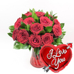 A richly romantic arrangement dominates this image, featuring a lush cluster of deep red roses rising from a ruby-red glass vase. Around a dozen or slightly more roses have been carefully placed so their heads form a generous dome, some blossoms fully open in sumptuous spirals, others half-unfurled with a promise of more beauty to come. Their petals look thick and velvety, the kind of texture you imagine brushing gently with your fingertips, while their colour is a saturated crimson that suggests classic, cinematic romance. Between the blooms, abundant dark green foliage weaves in and out, its surfaces slightly glossy, framing the roses and giving the design a sense of fullness and balance. The vase itself is made from clear red glass with a softly fluted design, so that subtle vertical ridges catch the light and create delicate highlights and shadows. It feels substantial yet elegant, like something chosen with care from a trusted local florist in Epping to grace a dining table after a proposal at Epping Forest or a special dinner near the High Street. In the lower right foreground, overlapping the base of the bouquet, a shiny red heart-shaped foil balloon adds a playful flourish. The heart's metallic finish gleams, and across its centre, in bold white cursive, the message I Love You is written clearly and confidently. A silver Cupid-style arrow appears to pierce the balloon diagonally, reinforcing the theme of love and romantic devotion. Set against a crisp, solid white background, every red and green detail stands out with striking clarity, creating an image that feels perfect for Valentine's Day surprises, anniversary deliveries, or heartfelt declarations sent across Epping and the neighbouring villages.