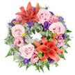 This full, circular funeral wreath is displayed on a pure white background, allowing every colour and texture to stand out clearly. The design forms a lush, unbroken ring of flowers, suggesting completeness and the unending nature of love. Two striking orange-red Asiatic lilies anchor the composition, one towards the top and one nearer the lower edge, their wide, star-shaped petals open to reveal prominent stamens at the centre. Around them, clusters of light and blush pink roses are carefully arranged, each rose blooming in gentle spirals that bring softness and a feeling of heartfelt sympathy. Interspersed among the roses are lisianthus in shades of pale pink and deep lavender-purple, their ruffled, cup-like blooms filling spaces and adding layers of texture. Fine sprays of tiny, lavender-blue filler flowers weave through the design, giving a misty, airy quality much like the soft haze that sometimes settles over Epping Forest. Beneath the flowers, a generous bed of mixed foliage provides structure and contrast: silvery-green eucalyptus leaves, darker glossy greens, delicate fern fronds, and spiky blue eryngium thistles combine to create a rich, varied background. A few closed lily buds are tucked quietly among the leaves, hinting at future blossoms and the continuation of cherished memories. Some broader, striped green leaves have been artfully folded and positioned near one of the main lilies, adding a modern, crafted touch that reflects the skill of local florists serving families across Epping, Theydon Bois, and the surrounding villages. The wreath's overall impression is one of dignified beauty and gentle comfort, perfectly suited to honour a loved one at a funeral, memorial, or graveside tribute.