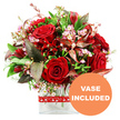 An elegant, hand-crafted bouquet of rich red flowers sits proudly in the centre of a pure white background, its colours and textures carefully composed to tell a story of romance. At the core, velvety red roses cluster together, some in tight buds hinting at new beginnings, others open and generous, revealing layer upon layer of soft petals. Nestled among them are smaller, deep scarlet blooms similar to alstroemeria and carnations, their many petals and speckled interiors lending detail and a lively rhythm to the design. Fine stems of pale pink and white waxflower are delicately woven through the arrangement, their tiny, dainty flowers and rounded buds adding a soft, airy lightness that balances the passionate reds. Around the outside, lush green foliage fans out-glossy dark leaves, lighter green tips, and standout foliage in burgundy and copper-red tones, some finely veined, which adds depth, contrast, and a slightly dramatic flourish. The bouquet is arranged in a modern, clear glass vase with a clean rectangular base, its transparent sides allowing a glimpse of the stems and water for a fresh, contemporary look that would feel at home in an Epping apartment overlooking Station Road or a traditional house near Epping Forest. A bright red ribbon printed with neat white heart outlines is tied snugly around the vase, instantly suggesting Valentine's Day, an anniversary, or a heartfelt I love you. In the lower right corner of the image, a bold orange circle bears the words VASE INCLUDED in sharp white capital letters, clearly indicating that this lavish, gift-ready arrangement arrives exactly as pictured, perfect for local flower delivery in and around Epping.